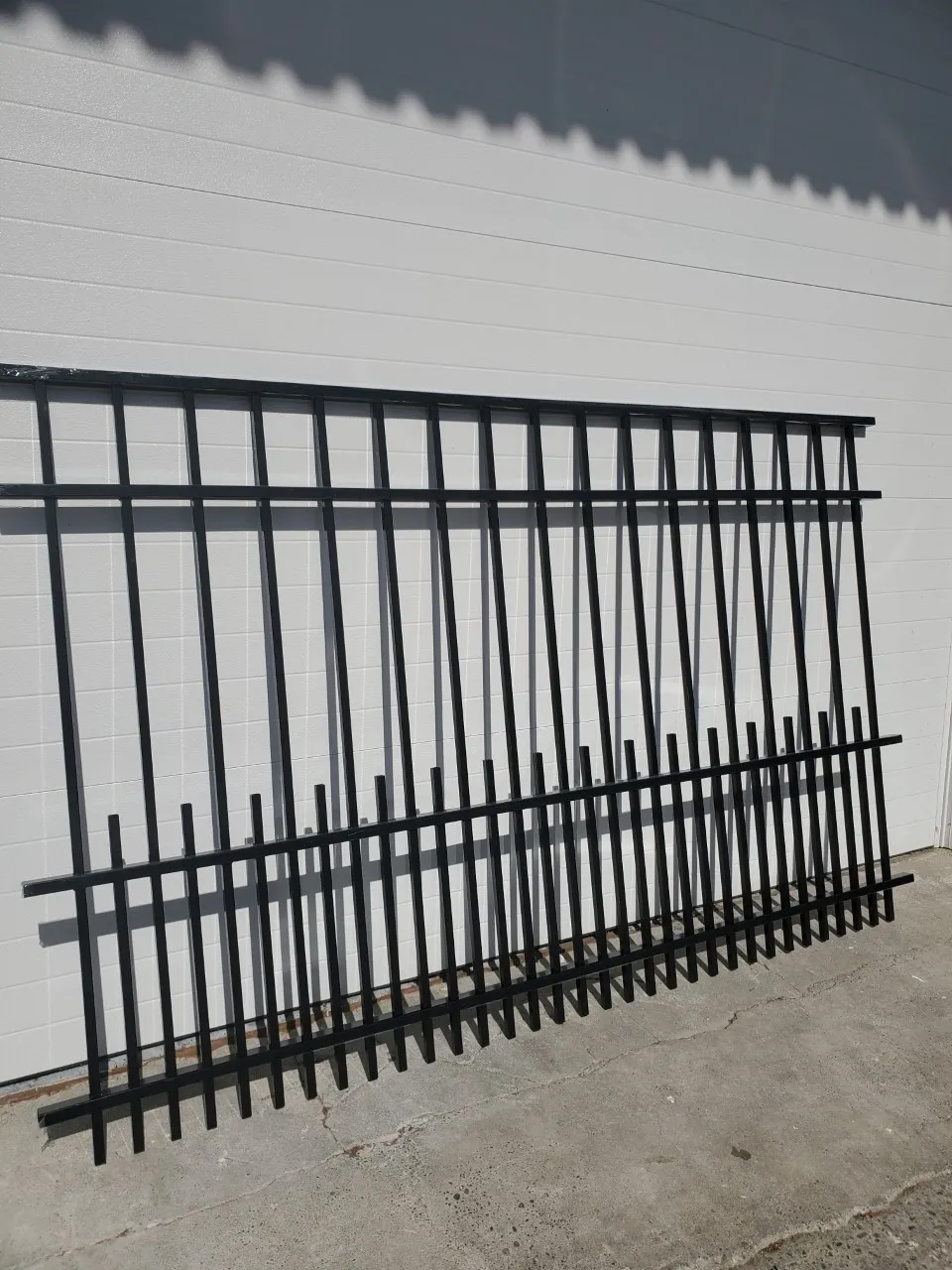 Black metal fence panels against white wall.