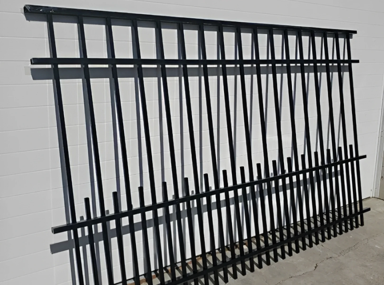 Black metal fence leaning against white wall.