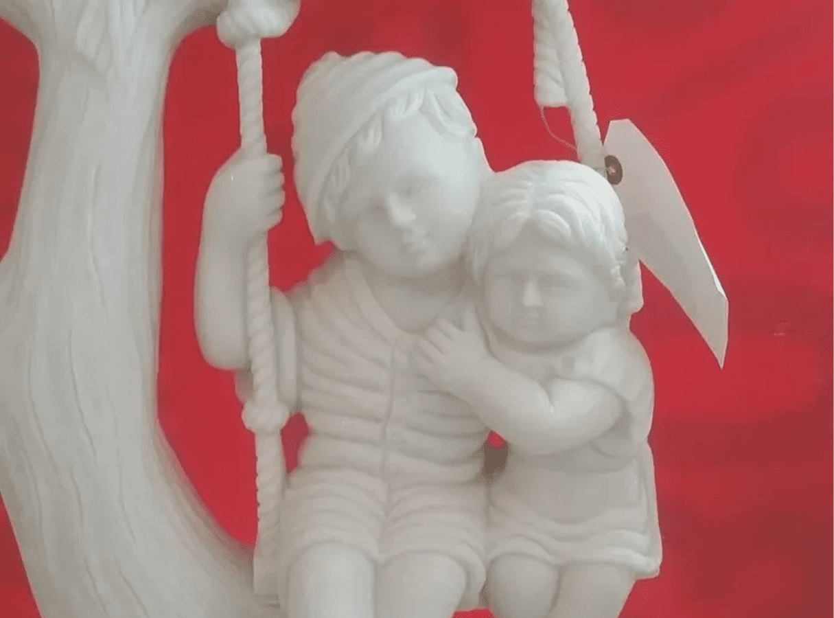 Children statue on swing, red background.