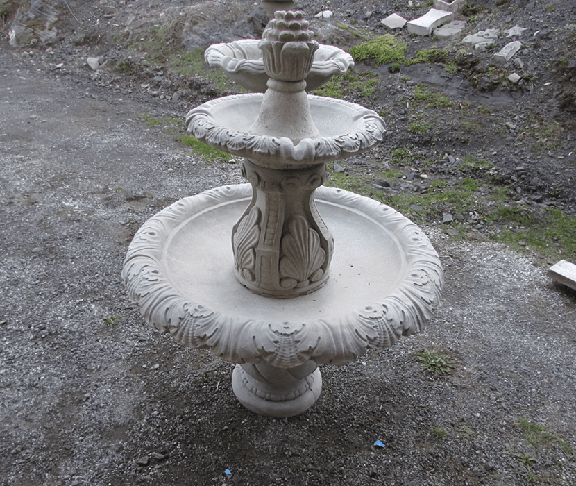 Stone tiered fountain on gravel ground.